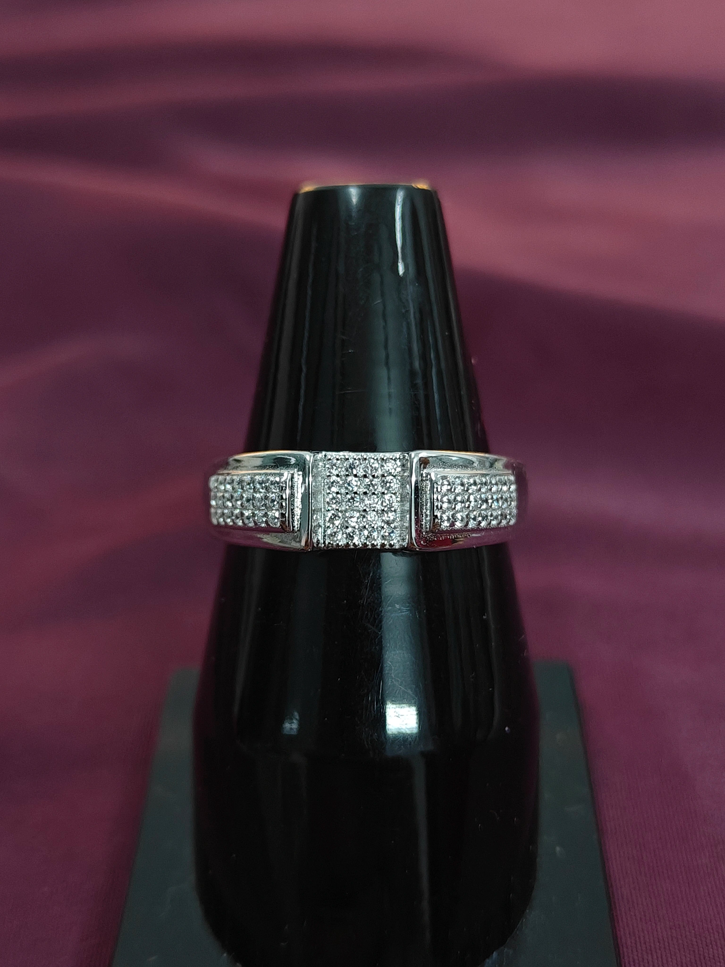 Silver ring with diamonds on a black stand against a purple background